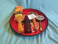 Overview photo showing all items in the lot: red round metal beer tray and four unique beer tap handles.