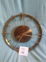 Front view of the round metal clock with open frame and atomic design hour markers.