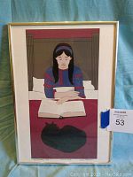 Framed lithograph showing full image of a young woman reading with a black cat curled on the table in front of her.