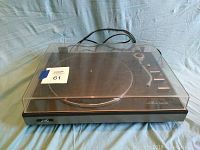 Photo of JVC JL A20 turntable with closed clear dust cover showing the whole unit on a blue cloth background.