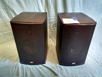 Pair of black PSB Alpha B1 speakers shown side by side on light background. Minor blemishes visible on top surfaces.