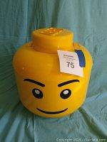 Front view of the large yellow LEGO head container with lid on green background