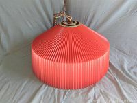 Front view of coral pleated lampshade with brass hanging chain and fixture.