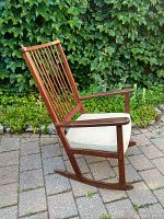 Side view of teak rocking chair on patio, showing curved rockers and armrests