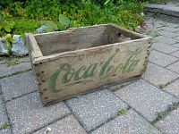 Wooden vintage Coca-Cola crate with green logo on long side, showing weathered wood and wear.