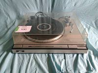 Front view of the JVC L-A55 turntable with transparent dust cover closed, showing control buttons and black record platter beneath.