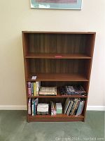 Front view of the teak bookcase filled partially with books on the bottom shelf.