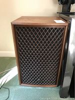 Vintage wooden speaker with lattice grill front panel, on carpeted floor