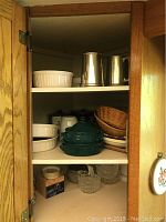 Open cupboard shelf showing three Birks pewter beer mugs, white Corning Ware serving bowls, small glass bowls, crystal coasters, wicker bowls.