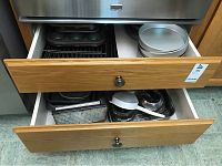 Two kitchen drawers open showing a collection of baking pans, tins, racks, and plates in layered arrangement.