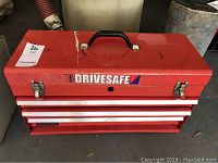Closed red metal Drivesafe tool box with 3 drawers, showing handle on top and latches on front.