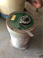 Side view of round in-ground safe showing cylindrical rusty metal body and green top with combination lock and key lock