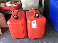 Two red plastic gas cans standing upright with black and yellow screw caps, showing front and side views.
