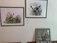 Two framed floral art prints hanging on wall, one featuring a watering can with flowers and bird, the other with various flora and a yellow bird