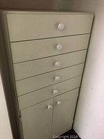 Front view of wood cabinet showing five drawers with round white knobs and lower cabinet doors.