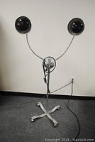 Full frontal image of the mid-century heat lamp showing the chrome central sphere with two curved gooseneck lamp arms, connected to a wheeled X-shaped base.