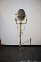 Full view of the 66-inch tall brass floor lamp with oval mirror and two light bulbs