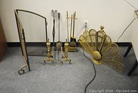 Overall photo showing the brass peacock tail fireplace screen, steel center-hinged fireplace screen, and fireplace accessories including andirons, tool stand with shovel, broom, and poker, owl-handled shovel, and log tongs.