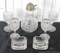 Full view of the syrup pitcher, four wine stems, and two open salt cellars arranged on a black surface.