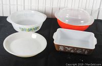 Full lot of 4 casserole and pie plates on black cloth with white tile background.
