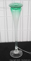 Full view of the tall green art glass vase against a gridded white background and black surface, showing its height and shape.