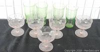 Four green raindrops pattern tumblers and five pink diamond quilted dessert/sherbet glasses on a black surface.