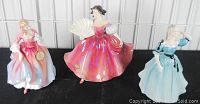 Three Royal Doulton figurines displayed together showing dresses and figurine details.
