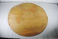 View of the full circular flat globe map laid flat, showing the world map with continents and ocean details, exhibiting wear and aging.