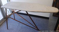 Side view showing wooden legs, foldable structure, and padded, cream-colored fabric cover on ironing board