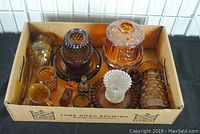 Eight-piece set of glassware in a cardboard box including amber and brown fairy lamps, small pitchers, toothpick holders, and figurines.