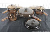 Full set view of amber Pyrex Vision cookware including skillet, saucepans, and lids on black surface.