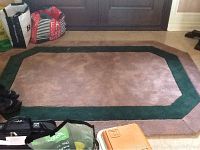 Full view of the mauve carpet with dark green border laid flat on floor surrounded by bags and shoes.