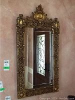 Front view of the ornate wall mirror showing engraved glass and decorative metal frame with floral and scroll designs.