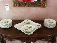 Set of stacked plates and serving pieces arranged on ornate wooden table, showing overall lot contents