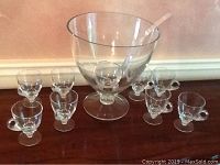 Full view of glass punch bowl with eight small glass cups arranged around it on a table.