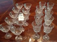 20 Royal Doulton crystal glasses arranged on wooden table showing both wine and sherbet glasses with intricate cut crystal design and starburst bases.