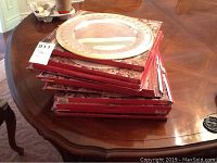 Stack of red-edged Museum ReCreations boxes on a wooden table topped by a silver plated charger plate
