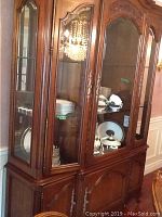 Front view of the wooden china cabinet with glass-paneled upper doors showing shelves with dishware inside.