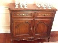 Front view of the wood bar cabinet showing two drawers with brass fittings and two paneled doors below, carved base detail.