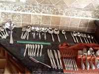 Full layout of flatware on countertop showing multiple forks, spoons, knives, and serving utensils.