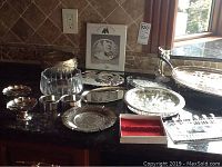 Wide view showing the arrangement of various silver serving pieces including footed bowls, trays, candle sticks, and boxes with cheese markers and pickle forks.