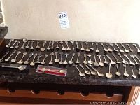 Overview of 63 collector spoons arranged on a table displaying variety in shape and design.