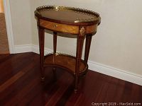 Front view of oval side table showing inlaid top, drawer and brass gallery rail