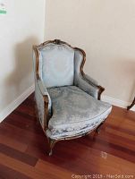 Full view of easy chair showing carved wood frame and light blue floral upholstered seat and back.