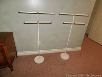 Photo of both white metal towel stands showing their full height and placement next to a cabinet.