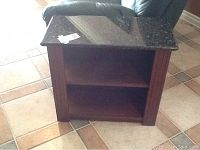 Front view showing black marble top, open shelving, and solid wood base with decorative vertical fluted details on the sides.