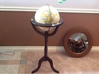 Full view of 12 inch globe on dark wooden stand and round wood framed mirror on floor