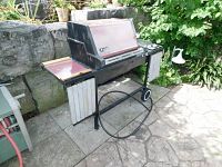 Front and left side view of natural gas BBQ showing maroon lid, wooden-edged side shelves, gas hose.