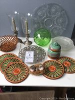 Wide view of the lot showing 2 Gorham sterling candle holders with glass hurricane shades, etched plates, ceramic lidded pot, green glass vase, woven basket, metal trivet, placemats, and bird decoration.