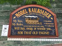 Full view of arched wooden wall sign with text 'MODEL RAILROADER' and decorative raised metallic locomotive in center, placed on outdoor surface with ruler for scale.